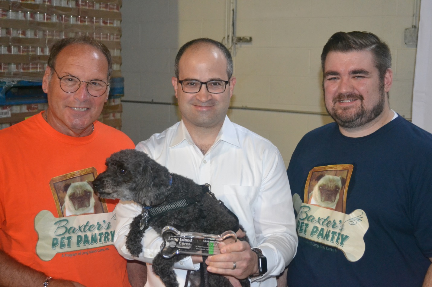 Assemblyman Ra (center) and his rescue dog, Carter, accept an award from Long Island Cares CEO, Paule T. Pachter (left) and Community Events and Food Drive Manager, Billy Gonyou (right) for their part